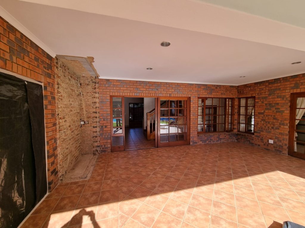 Original patio showing an exposed brick feature wall and terracotta tiled floor before renovation.