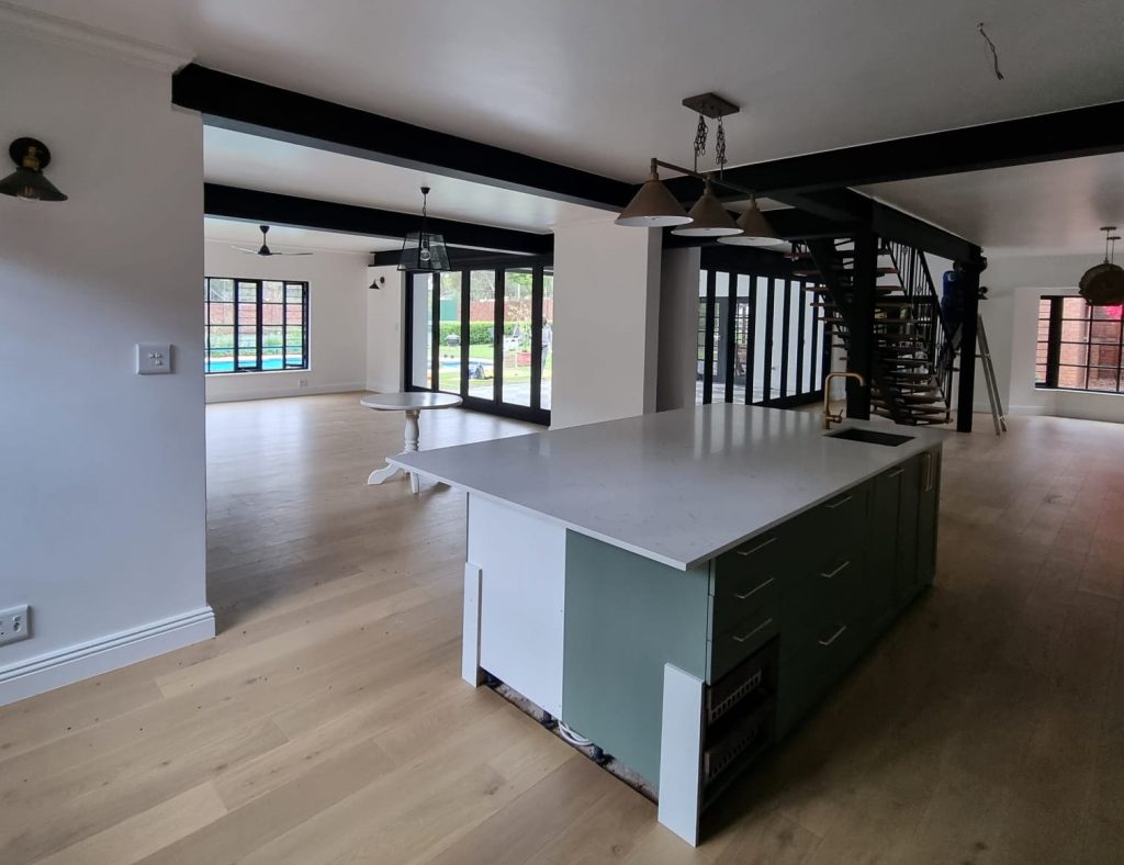 Renovated kitchen and living space with a central island and exposed steel beam overhead.