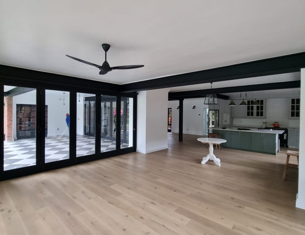 Open living area with timber flooring beneath an exposed steel ceiling beam.