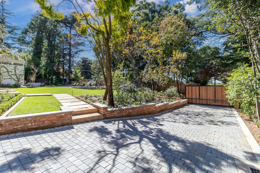 Paved driveway and courtyard bordered by a brick retaining edge and mature garden trees.