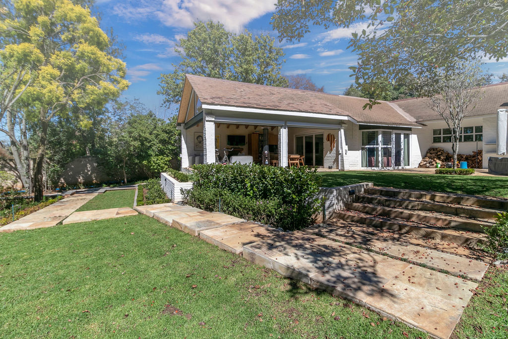 Side view of the home with a covered patio, stone steps, and a sloped lawn.