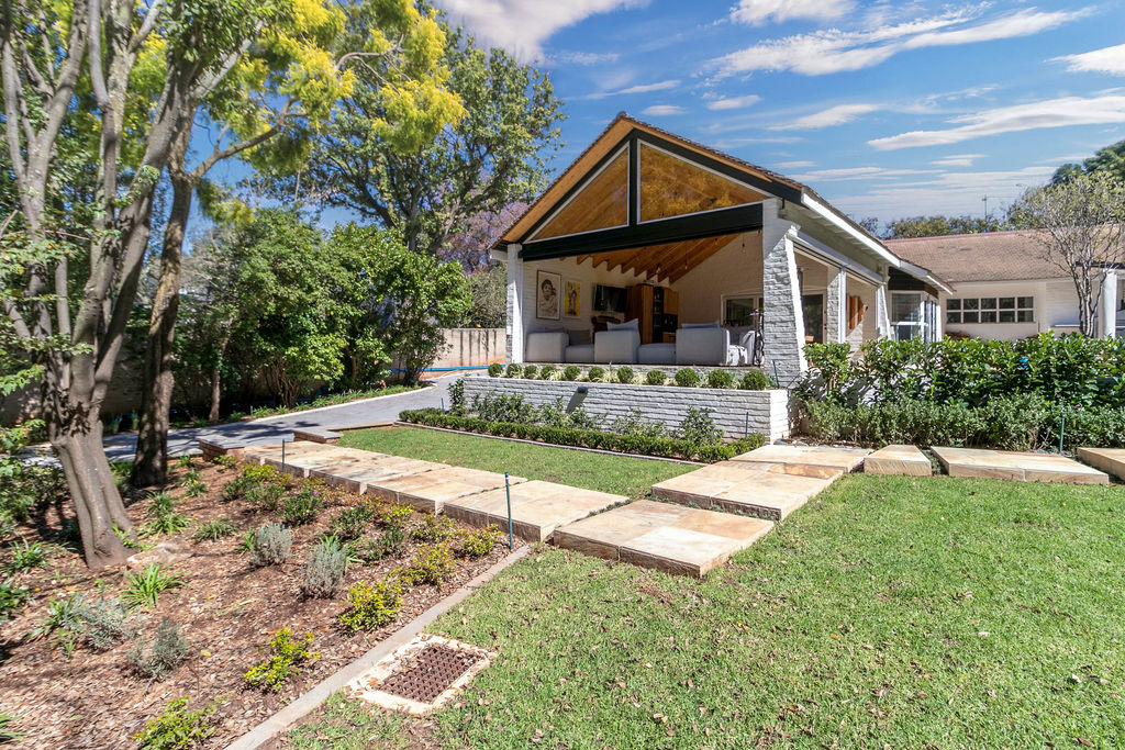 Front approach showing the gabled patio addition set behind a tiered garden and paved path.