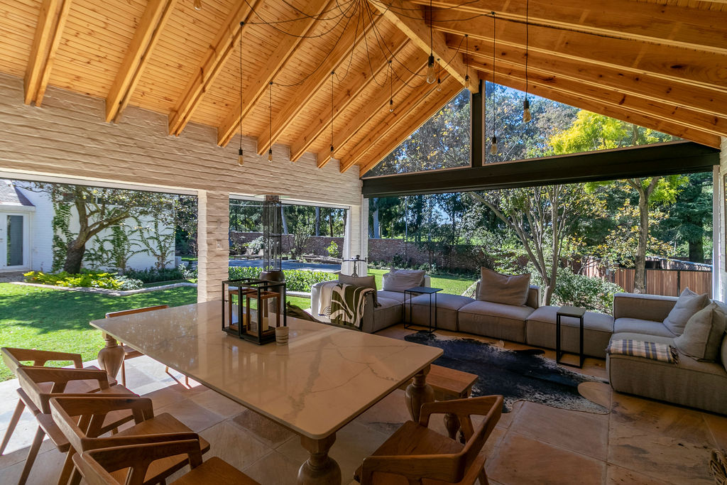 Interior of the covered patio with vaulted timber ceiling, dining table, and lounge seating open to the garden.