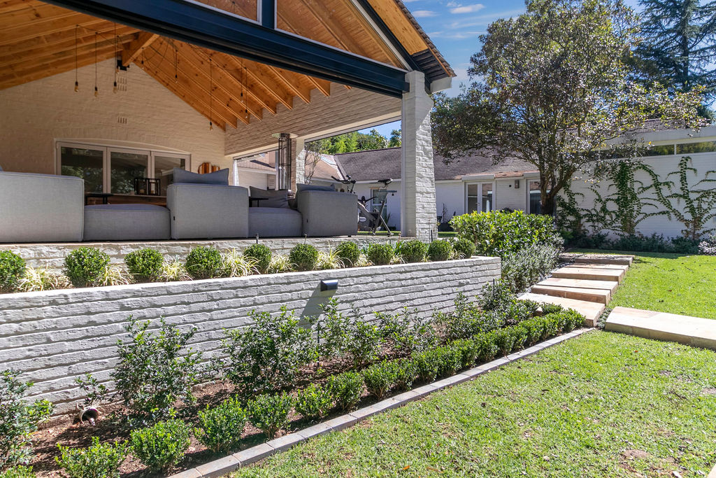 Covered patio and stepped lawn viewed across the tiered stone retaining wall and border planting.